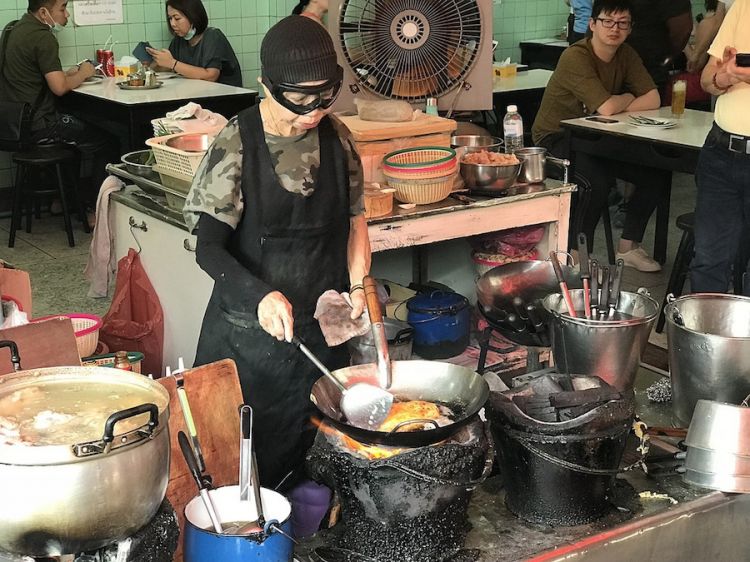 Jay Fai, leggenda dello street food tailandese, in pieno servizio nella cucina della sua bottega a Bangkok. Un posto così in Italia difficilmente aprirebbe. Per la Michelin vale una stella
