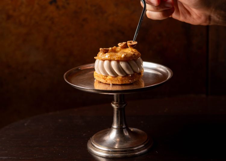 Le celebrazioni si estenderanno anche alla Farmacia Del Cambio, laboratorio di pasticceria, caffè e boutique gastronomica: è così che nasce la monoporzione Torino-Parigi (nella foto), disponibile dal 5 ottobre. Alla base dell’idea c’è Torino, la città di Del Cambio, la sua storia, il Piemonte e la nocciola, che qui diventa il cuore del dolce, attraverso il pralinato e la mousse. Parigi rappresenta invece la tecnica francese della Paris-Brest, a cui si ispira il dessert. Il nome racconta quindi l’incontro tra le due città, legate storicamente da un dialogo culturale e gastronomico molto forte. L’arancia, con il gel e le zeste semicandite, porta freschezza e contrasto con la nocciola, dando una nota contemporanea al dolce