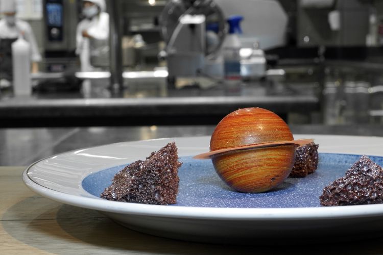 Universo: sul fondo un burro di cacao, le "rocce" sono di cioccolato fondente soffiato, Saturno è composto come un Foresta Nera, con mousse di vaniglia di Tahiti, cuore alla ciliegia e pasta frolla al cioccolato
