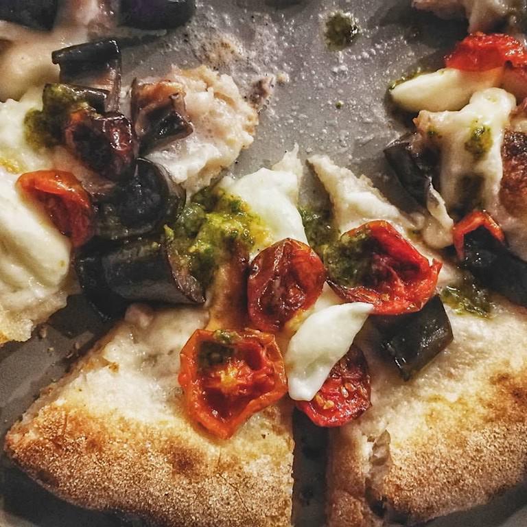 Una pizza di Ciro Carbone all'Ossteria: è condita con melanzane fritte, provola affumicata, pomodorini Pachino arrosto e pesto al basilico
