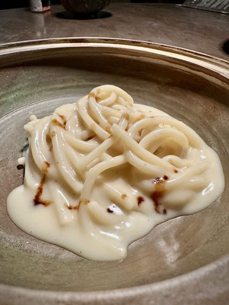 Il risultato finale: Pici all'acqua di pomodoro. Vengono usati 27 tipi diversi di ortaggio (in passato erano 5 varietà), dopo aver realizzato tante prove sulla profondità dell’acqua di pomodoro. Essi sono setacciati, in modo da estrarne solo l’acqua e i succhi, per riprodurre una sensazione simile al morso del pomodoro crudo. Tale operazione non è puramente estetica o per l’effetto cromatico (sono in bianco), ma per trattenere acidità e freschezza nel liquido, in modo da non far partire l'ossidazione. Tra gli altri elementi, abbiamo la cottura su braci di olivo, piante dove i pomodori si arrampicano spontaneamente. C'è un tocco di Aceto balsamico Modena 50 anni, che gioca con balsamicità dell'olivo e l'acidità e la dolcezza del pomodoro. Infine, la pasta: i pici, autoprodotti, hanno tanto amido (ideale per la mantecatura), grazie alla farina di tipo Senatore Cappelli, coltivata sempre da loro