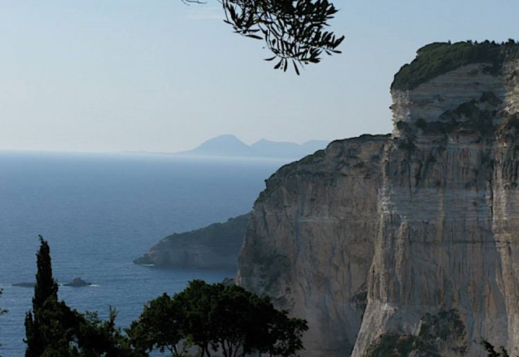 Se le spiaggie più accessibili di Paxos sono sulla costa orientale, quella che guarda la Grecia, nulla supera la spettacolarità della costa occiddentale, quella verso il mare aperto con le sue scogliere di oltre diecento metri a picco sul mare. La foto strega, sulla sfondo si distingue Corfù distante circa 24 km
