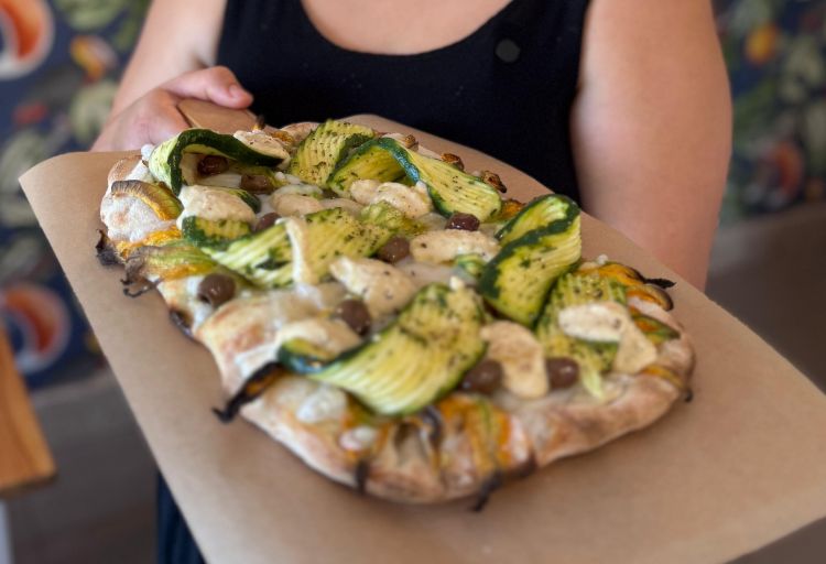 Pinsa con zucchine marinate, fiori di zucca, formaggio vegetale e olive