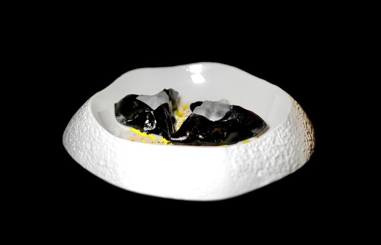 Raviolo nero: ravioli neri farciti con seppia, bambu e curry, serviti con velo di seppia, latte di cocco profumato allo zenzero e lemongrass