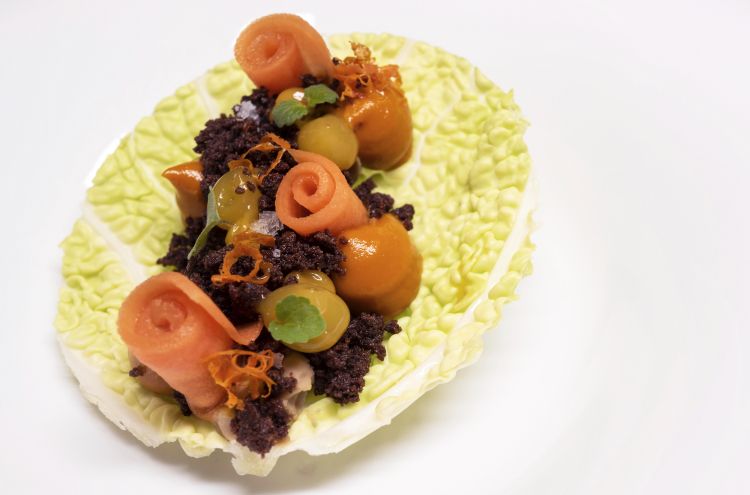 Carota, mandarino e liquirizia: a racchiudere la cremosità di questro dolce vegetale, una foglia di verza che raccoglie consistenze di carote, un crumble al cacao e deliziosa liquirizia che, con i suoi sentori balsamici, condisce le verdure e rinfresca il palato