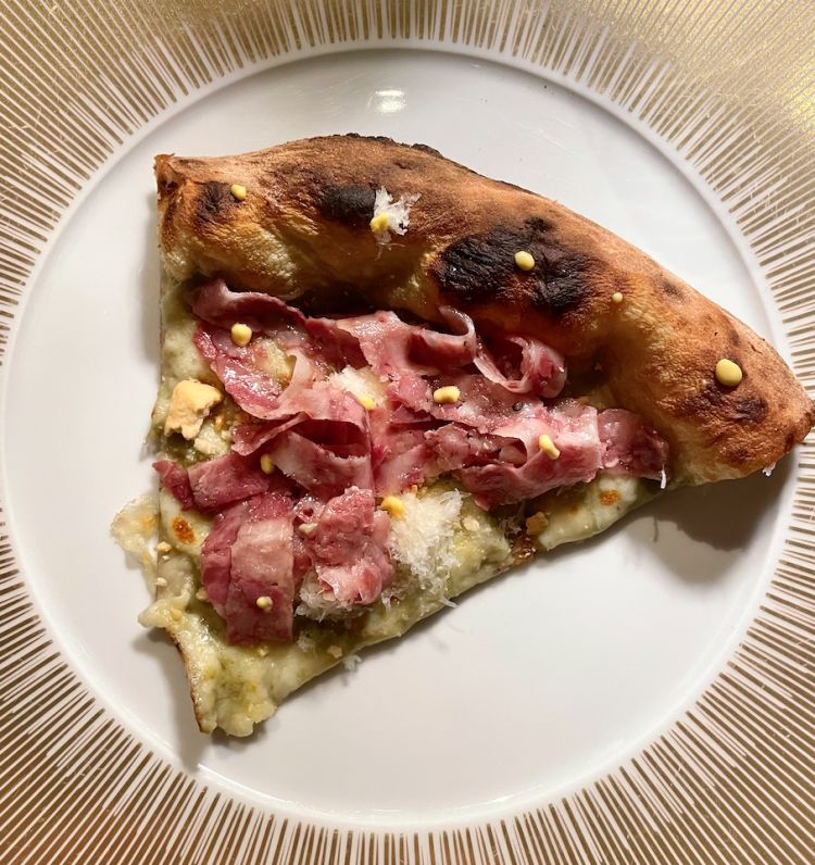 Tagliatella di coppa di Alex Lo Stocco - Fior di latte, crema di carciofo spinoso di Sardegna, coppa di testa, crumble di tarallino, senape di Digione e provolone del monaco stagionato su impasto con farina al germe di grano.
Ci spostiamo sul fronte della pizza contemporanea, dal cornicione sviluppato, una base ragionevolmente estesa, ma il profumo è quello di una volta, di forno, di semplicità; una pizza dal gusto rustico; la base viene condita con crema di carciofo, dolce, delicata, fior di latte e, in cima, coppa di testa tagliata a mo’ di “tagliatelle”, la cui grassezza viene attutita da punti di senape qua e là, mentre il crumble di tarallo apporta sonorità, in perfetto stile Lo Stocco. Un assaggio ben bilanciato in cui avremmo voluto sentire di più il carciofo