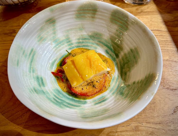 L’Haddock (in italiano eglefino) è un pesce della famiglia dei merluzzi. Viene affumicato ed è tipico del Nord della Francia e del Belgio. Passerini lo cucina confit in un olio arricchito dal carapace dell’astice, e lo condisce con peperoni arrosto, peperoncini dolci e pickled piccantini, shiso, pepe verde e una bisque di scampi e astice. Al gusto ricorda la nduja, senza che ci sia davvero!
