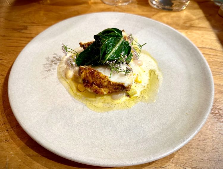 Rana Pescatrice alle spezie, ragù di mais, fagioli e fagiolini, bietole, fiori di coriandolo ed emulsione al Savagnin. Nella cucina di Giovanni Passerini le erbe, le spezie e i fiori hanno un ruolo fondamentale: spesso cambiano passo ai piatti, come in questo caso. La Rana Pescatrice, compatta e soda, senza un filo di grasso, è avvolta da un mix di spezie, esaltato ulteriormente dai fiori di coriandolo e dal Savagnin. Grande piatto
