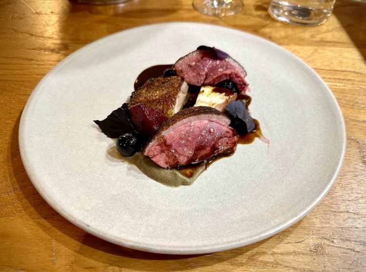 Anatra arrosto (proveniente dalla Maison Burgaud), cotta sull’osso intera, con il petto finito al barbecue e le cosce confit, melanzane arrosto in crema, barbabietole affumicate, mirtilli, jus di anatra all’aglio nero. Qui siamo di fronte a un grande omaggio alla cucina francese più classica, con un bel tocco vegetale per i contorni, che richiamano nei colori la carne, ma che sgrassano e ripuliscono il palato
