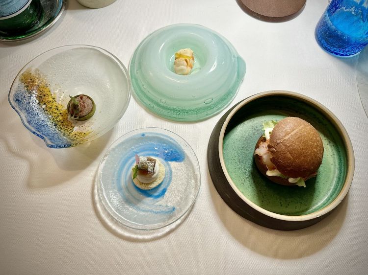 Il benvenuto da Scjabica: Canapè bianco con ricotta al pepe nero, alaccia affumicata, cipolla agrodolce, riduzione di agrumi; Tartelletta salata al basilico, patè di fegati di pesce e vermouth, polvere di peperone affumicato; Mazzancolla fritta e limone candito; Paninetto degli amici (pane al burro, molto morbido) con gambero rosso crudo di Scoglitti, emulsione al limone, misticanza e spezie
