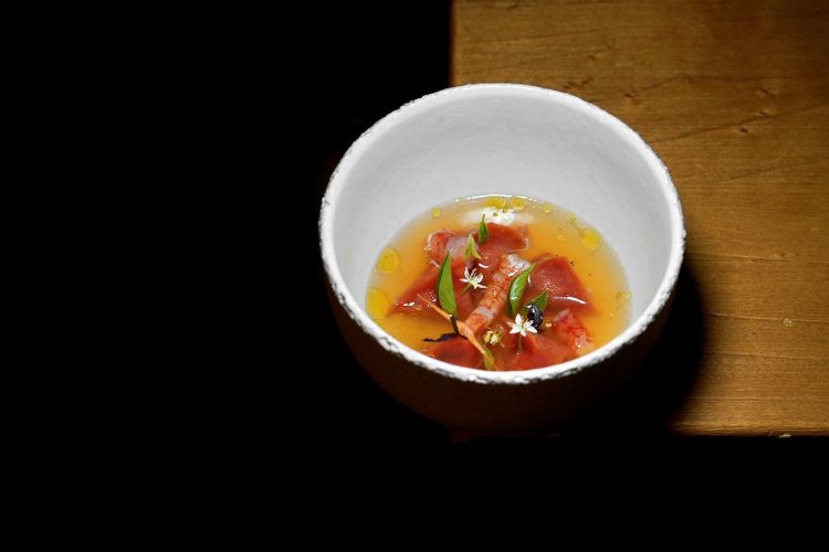 Pomodoro candito e pane casareccio uniti dolcemente in pappa a farcire i ravioli di pasta rossa, gambero rosso di Ortigia, brodo limpido ai profumi di grigliata di pesce
