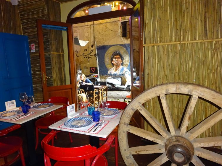 Dall'interno del Presepe Napoletano la vista spazia sui tavolini esterni su Vico Fico al Purgatorio e il murales di Diego Maradona