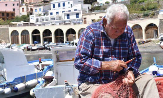 Un anziano pescatore ripara le reti nel porto di U