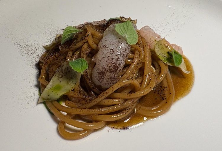 Spaghettone alla matticella, carciofi alla brace, mentuccia romana e crudo di scampi
&laquo;Lo spaghettone prende il nome dai carciofi alla matticella, una preparazione tipica del centro Italia. Le matticelle sono fasci di legnetti raccolti dai vignaioli dopo la potatura delle vigne: una volta seccati, formano una brace molto fina. I carciofi interi vengono aperti, farciti con aglio, prezzemolo e mentuccia, e inseriti in questa brace che vi aderisce completamente, dando un aroma intenso. Li cuociamo poi sottovuoto per quattro ore, frulliamo il tutto e lasciamo decantare una notte: otteniamo un brodo in cui cuociamo la pasta, che assorbe tutti i pigmenti neri. Completiamo con scampi crudi di Civitavecchia, mentuccia e petali di carciofo alla brace&raquo;
